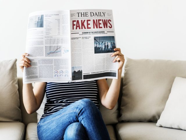 En person som läser tidningen med rubrik "Fake news".